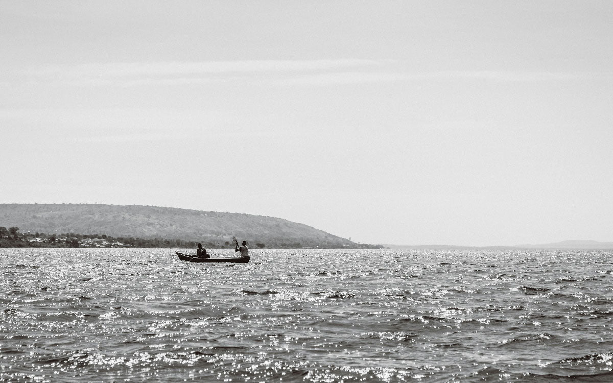 Two people in a small boat on open water with distant shoreline in the background